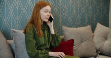 Evde cep telefonuyla konuşan üzgün genç bir kadın.