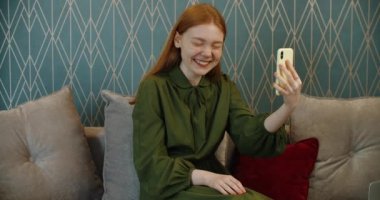 Kızıl saçlı genç mutlu kadın video iletişimiyle arkadaşlarıyla iletişim kuruyor..