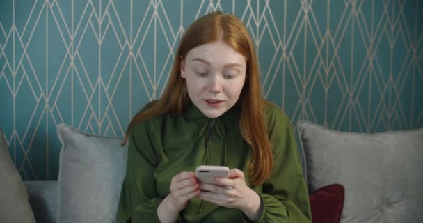 Emotions, surprise and joy. Emotional woman rejoices in victory, sitting on the couch at home, looks at the screen of a mobile phone. Win — Stock Video