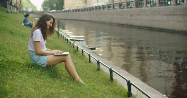 Donna bruna felice che lavora su laptop all'aperto seduta sull'erba nel parco. Bel posto dove lavorare. Freelance. — Video Stock