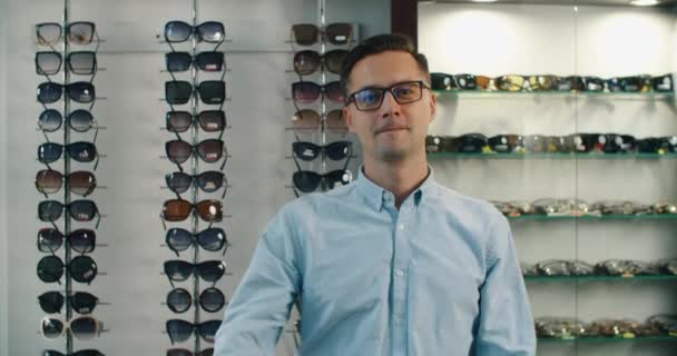 Die Wahl der Brille. Klient in der Optik. Selektiver Fokus. Der Mann blickt in die Kamera. Im Hintergrund steht eine Brille. Breites Sortiment im Geschäft. — Stockvideo