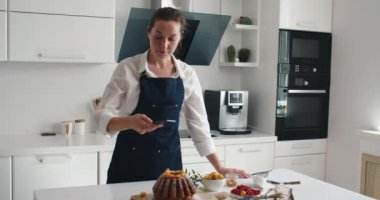 Blog için yemek fotoğrafçılığı. Kadın eli akıllı telefondan keklerin fotoğrafını ve videosunu çekiyor. Yemek blogcusu kek vuruyor. Yemek blogu. Seçici odak.