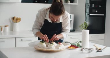 Taze böğürtlenli tatlı pişirme ve süsleme. Genç kadın pasta şefi mutfakta, tatlıyı böğürtlenlerle süslüyor. Mutfakta önlüklü mutlu kadın güzel doğum günü tatlısı yapar.