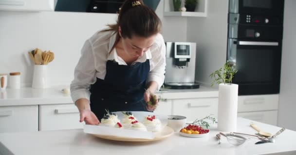 Приготовление и украшение десертов свежими ягодами и травами. Молодая женщина кондитер на кухне украшать десерт с berries.Happy женщина в фартуке на кухне делает красивый десерт день рождения — стоковое видео