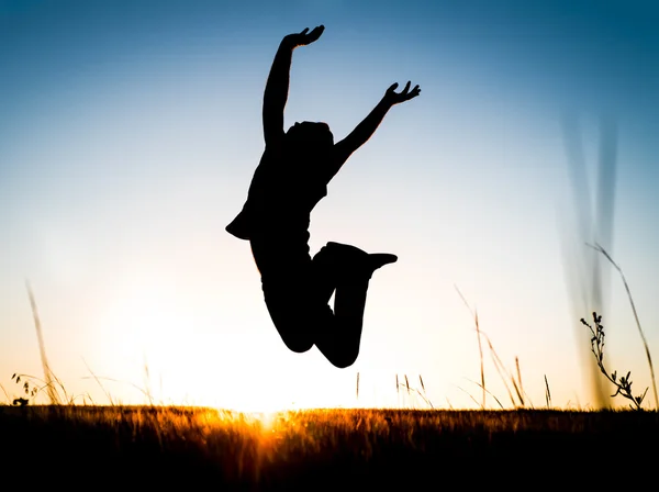 Silhueta do jovem feliz que salta sobre o prado — Fotografia de Stock