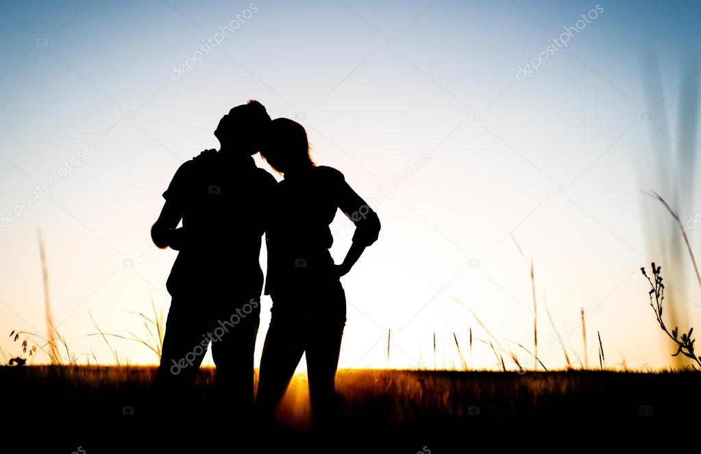 Happy couple silhouette on the meadow during sunset
