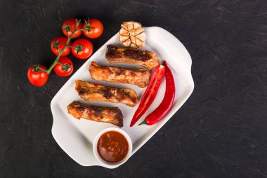 Beyaz tabakta dilimlenmiş domuz pirzolası, acı biber, kırmızı sos ve domates.