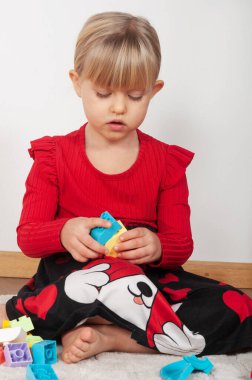 Sarışın bir kız, 4 yaşında, evde inşaat setiyle oynuyor.