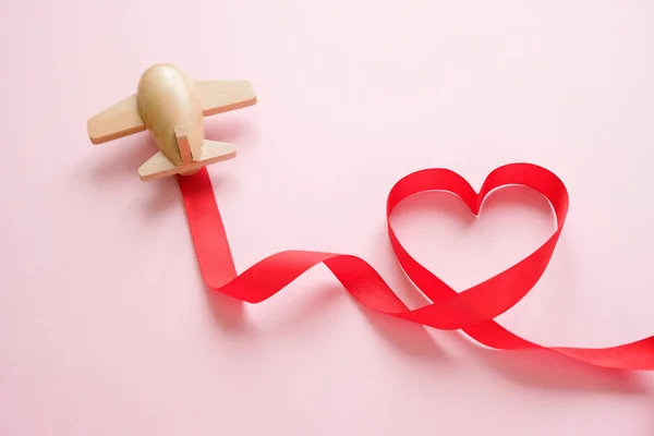 A small wooden toy airplane carries Valentine\'s elements. Vapor trail of sequins in the shape of heart, and red ribbon in the shape of heart. Valentine\'s day
