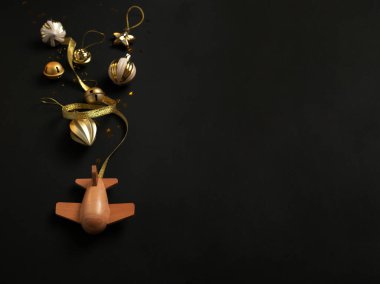 Siyah arka planda farklı noel süslemeleri olan ahşap çocuk uçağı. Mutlu noeller. Şanslı yılbaşı uçağı. Tatil bize geliyor.