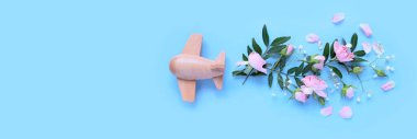 Tahta uçak ve çiçeklerle seyahat konsepti, mavi arka planda taç yaprakları. Üst manzara, düz yatış. Uzayı kopyala Seyahat, tatil konsepti.
