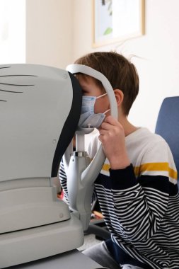 Optimetri uzmanı, modern bir klinikte bir hastanın oğlunu özel göz teçhizatlarıyla muayene ediyor. Çocuklarda vizyon düzeltmesi