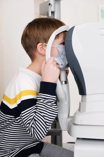 Optimetri uzmanı, modern bir klinikte bir hastanın oğlunu özel göz teçhizatlarıyla muayene ediyor. Çocuklarda vizyon düzeltmesi