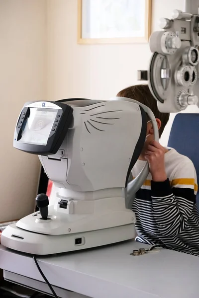 眼科医は 現代の診療所で特別な眼科機器を持つ患者の少年を調べます 子供の視力矯正 — ストック写真