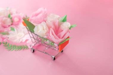 Bahar indirimi. Beyaz ve pembe kağıt çiçekli alışveriş arabası ve pembe arka planda yeşil yapraklar. Satış konsepti