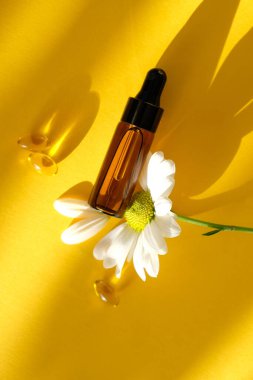 Roma papatyaları cam şişede, yağ kapsüllerinde ve sarı arka planda papatya çayı.