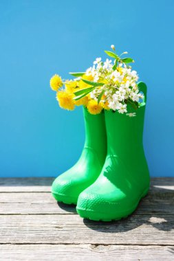 Merhaba, yaz konsepti. Mavi arka planda sarı çiçekli yeşil lastik çizmeler.