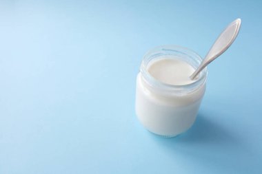 Açık mavi arka planda cam kavanozlarda ev yapımı Yunan yoğurdu. Seçici odak, boşluğu kopyala.