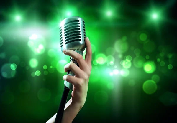 Female hand on blurred background holding microphone — Stock Photo, Image