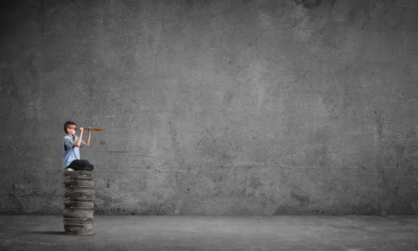 Kid on pile of books looking in spyglass — Stock Photo, Image