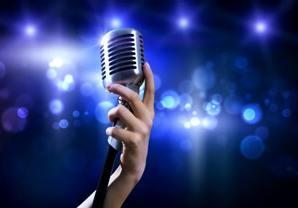 Female hand on blurred background holding microphone — Stock Photo, Image