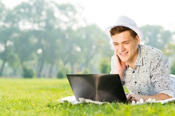 Giovane che lavora nel parco con un computer portatile — Foto Stock