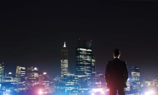 Бизнесмен смотрит ночной светящийся город
