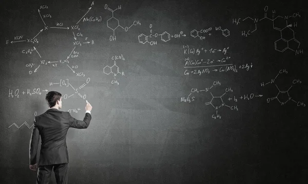 Young man drawing formulas on chalkboard — Stock Photo, Image