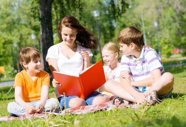 Professor lê um livro para crianças em um parque de verão — Fotografia de Stock