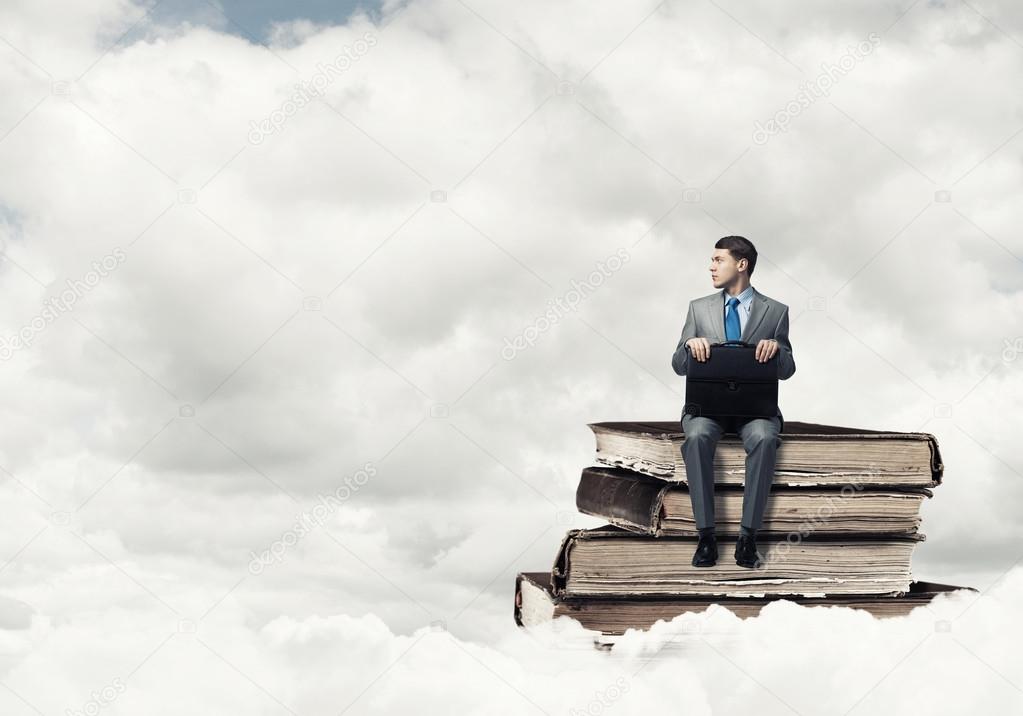 businessman sitting on pile of books