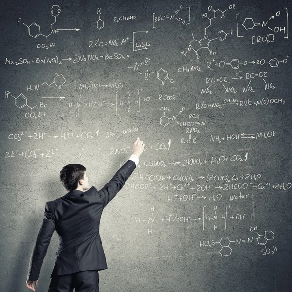 Young man drawing formulas on chalkboard — Stock fotografie