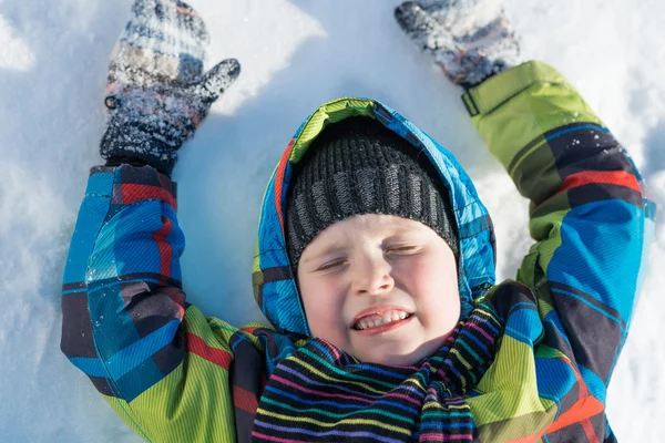 Menino bonito deitado na neve — Fotografia de Stock