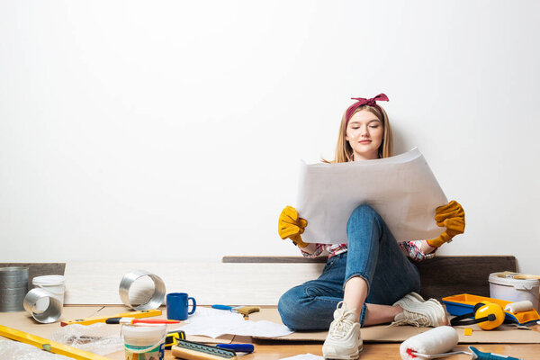 Happy woman sitting on floor with blueprint