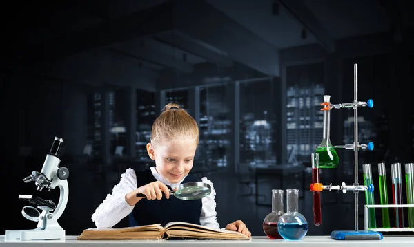 Klein meisje zit aan het bureau met vergrootglas — Stockfoto