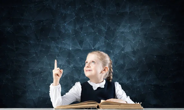 Smiling little girl sitting at desk with open book — Stock Photo, Image