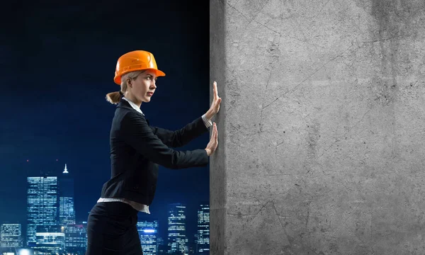 Beautiful woman architect pushing concrete wall