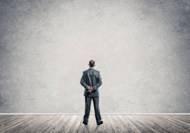 Elleri arkada olan ve boş beton duvara bakan bir iş adamı.