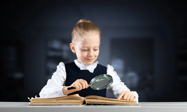 Liten flicka sitter vid skrivbordet med förstoringsglas — Stockfoto