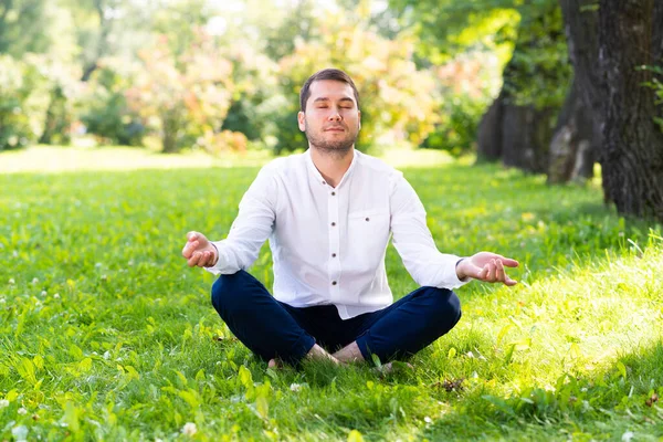 Young man meditates in lotus pose on green grass — Stock Photo, Image