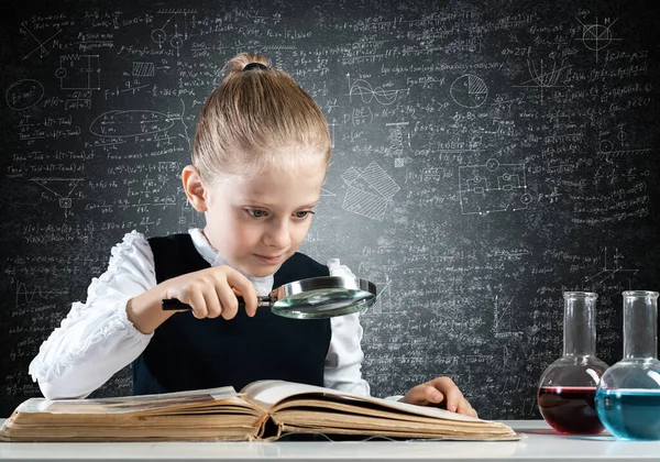 Klein meisje zit aan het bureau met vergrootglas — Stockfoto