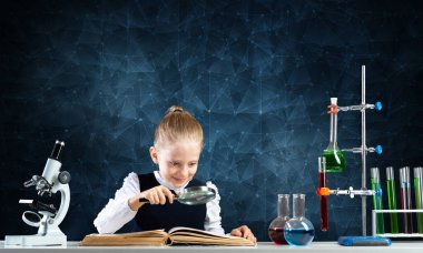 Küçük kız elinde büyüteçle masada oturuyor.