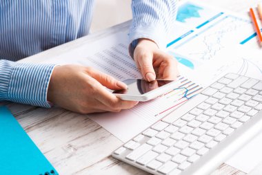 İş kadını cep telefonuyla masada oturuyor.