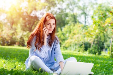Genç kızıl saçlı kadın yeşil çimlerde oturuyor.