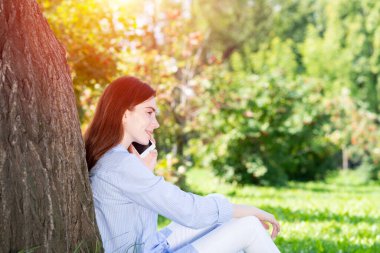 Genç kızıl saçlı kadın akıllı telefondan konuşuyor.