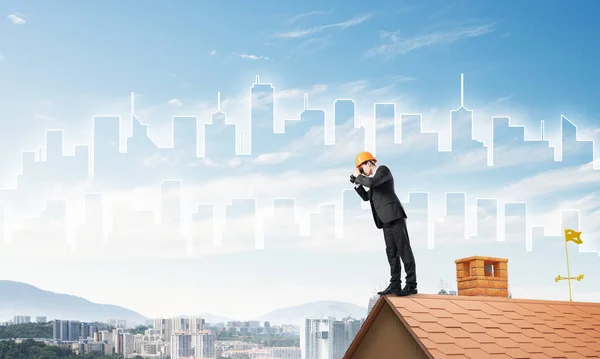 Ingegnere uomo in piedi sul tetto e guardando in binocolo. Mezzi misti — Foto Stock