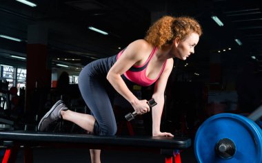 Spor salonunda dambıllarla nişanlı çekici genç bir kadın..