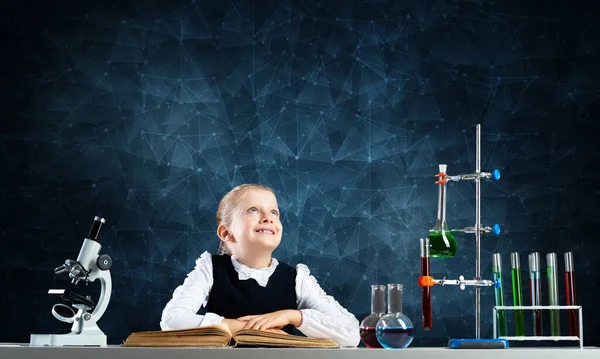 Smiling little girl sitting at desk with open book — Stock Photo, Image