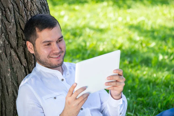 Homem usando tablet computador debaixo da árvore no parque — Fotografia de Stock