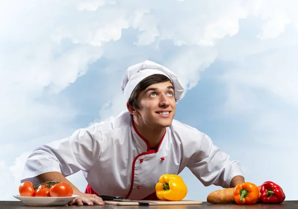 Jovem chef sorridente de pé perto da mesa de cozinhar — Fotografia de Stock