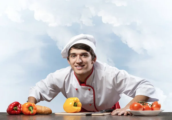 Jovem chef sorridente de pé perto da mesa de cozinhar — Fotografia de Stock